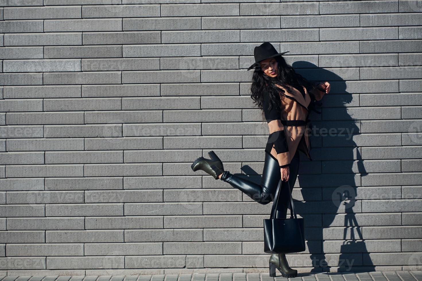 hermosa morena con el pelo rizado y vestida de negro camina al aire libre cerca de la pared foto