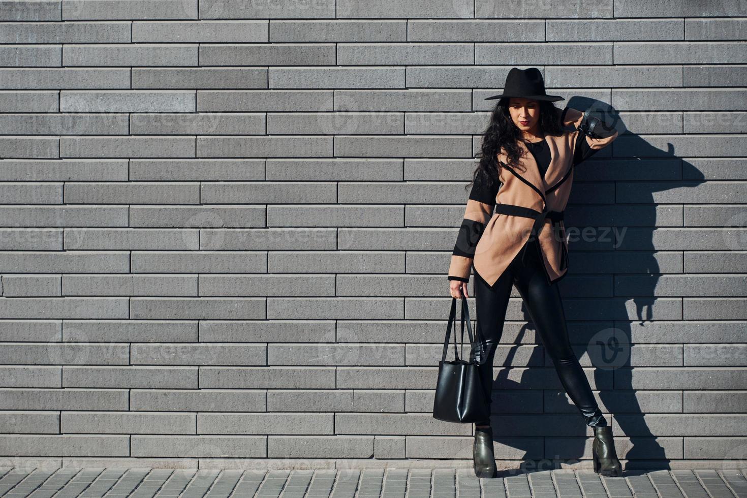 hermosa morena con el pelo rizado y vestida de negro camina al aire libre cerca de la pared foto