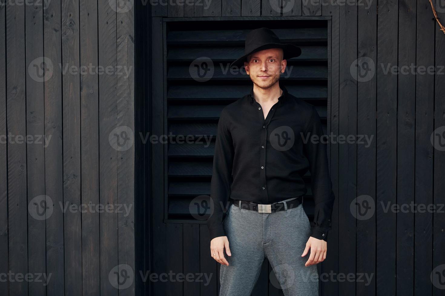 hombre con sombrero negro parado contra el exterior del edificio de madera negra foto