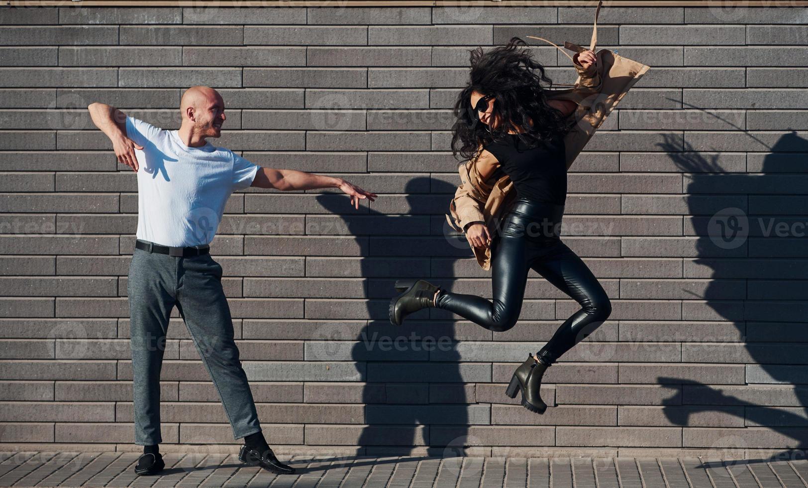 Beautiful couple in black clothes dancing together against wall outdoors photo