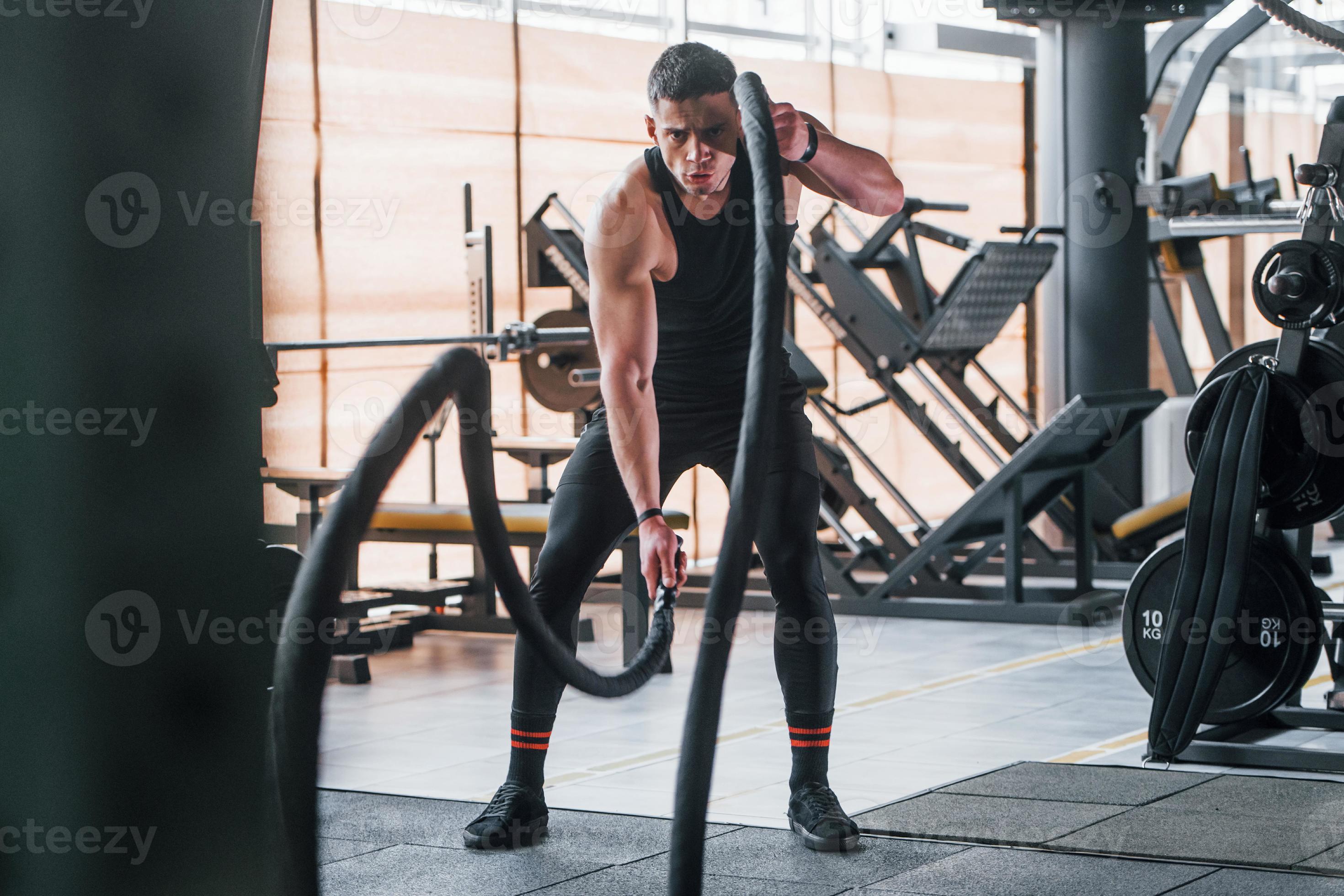 Exercising with knots. Young sportive strong man in black wear have