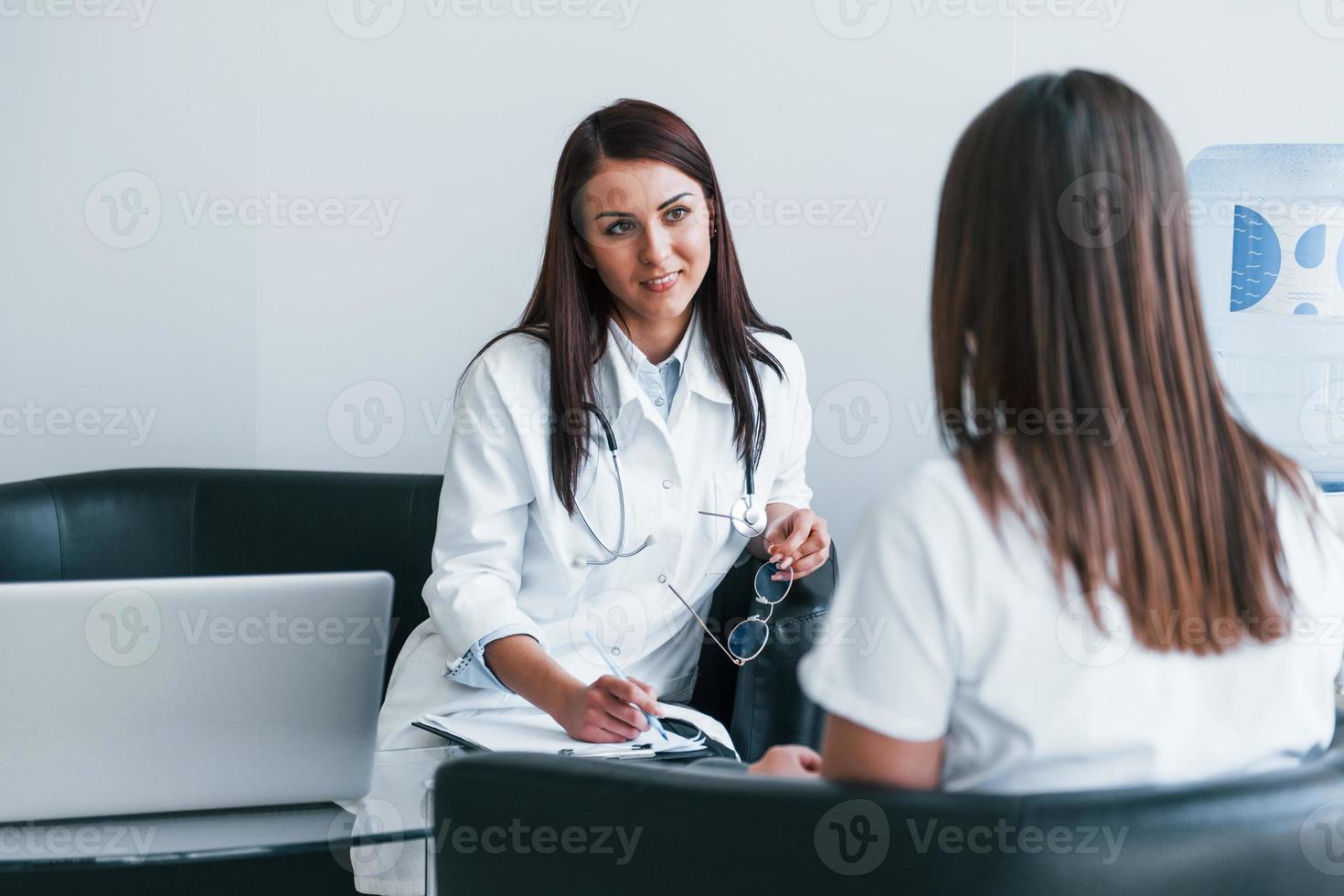 sentado y hablando. una joven visita a una doctora en una clínica moderna foto