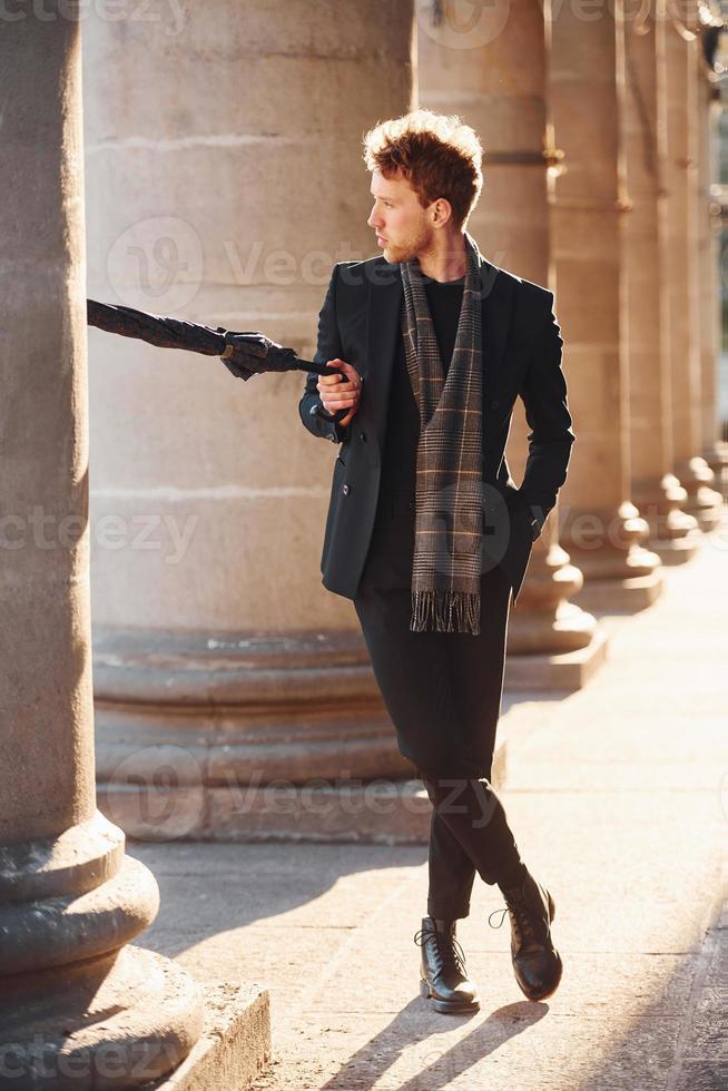 sosteniendo paraguas. joven elegante con ropa elegante y formal al aire libre en la ciudad foto