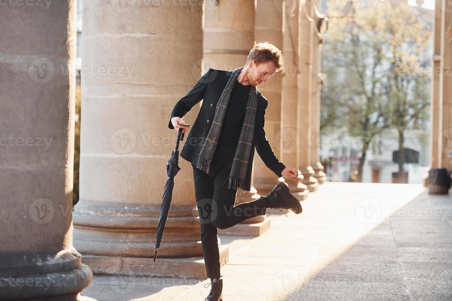 Holding umbrella. Elegant young man in formal classy clothes outdoors in the city photo