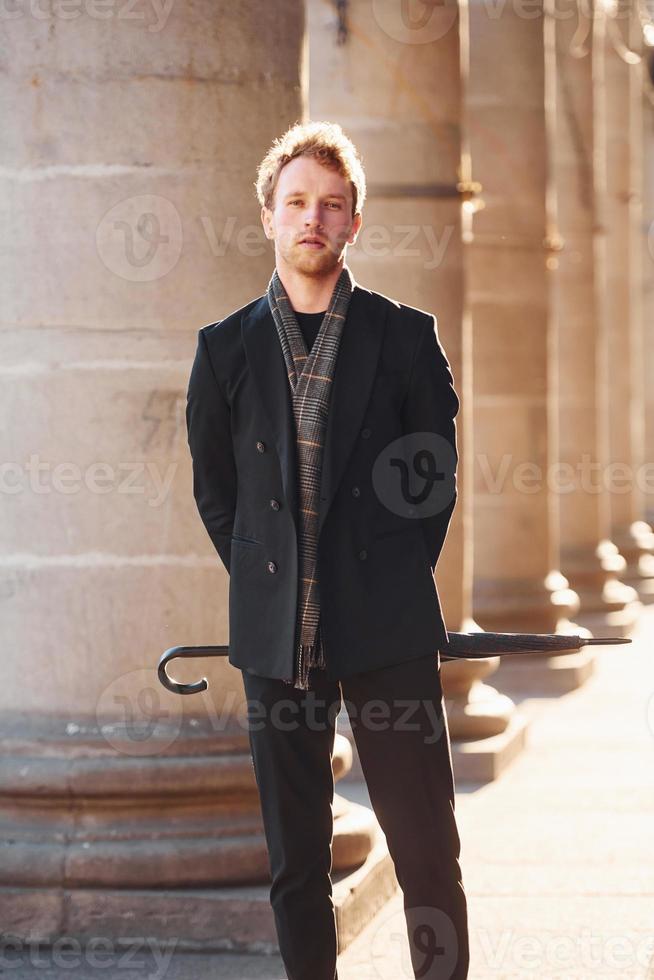 Holding umbrella. Elegant young man in formal classy clothes outdoors in the city photo