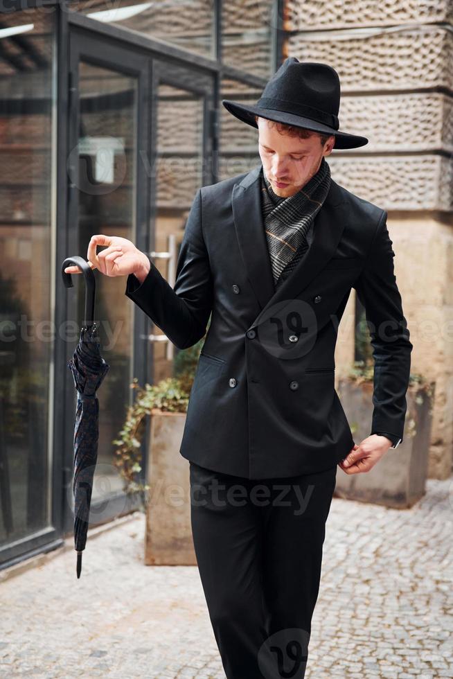 Hombre joven elegante en sombrero negro y ropa con paraguas en manos al  aire libre en la ciudad Fotografía de stock - Alamy