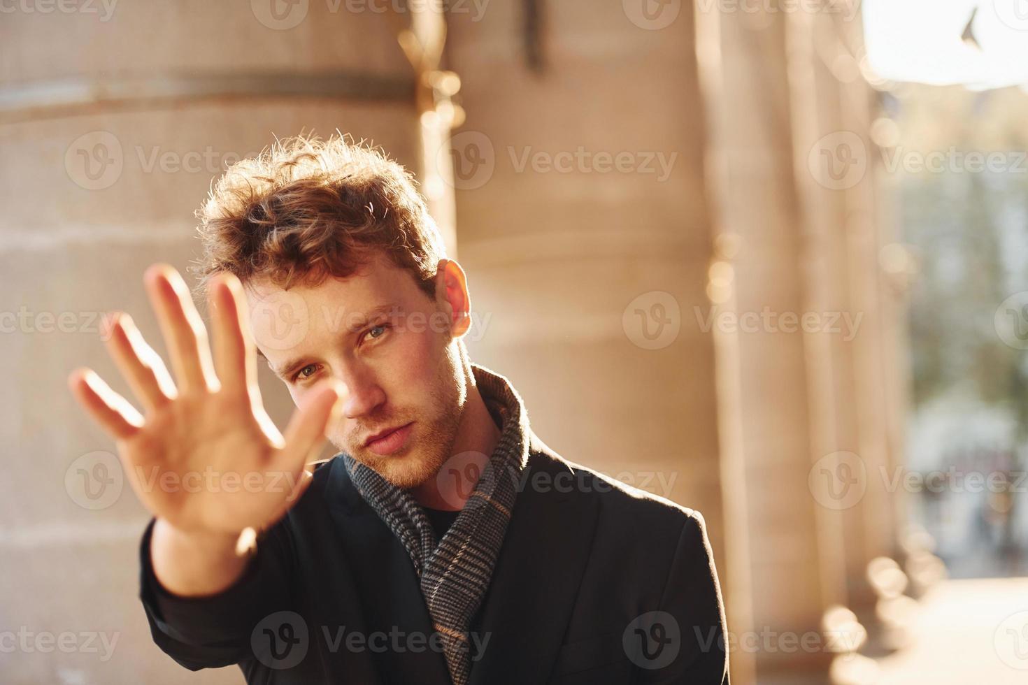 Shows stop gesture by the hand. Elegant young man in formal classy clothes outdoors in the city photo