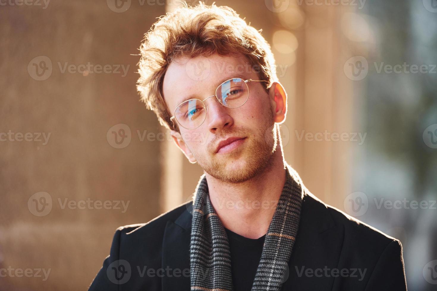 Portrait of elegant young man in glasses and formal classy clothes outdoors in the city photo