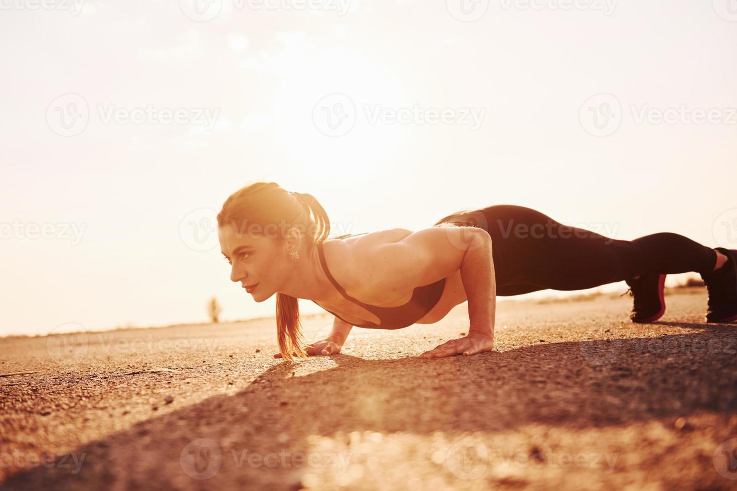 Woman in sportswear doing push-ups on the road at evening time photo