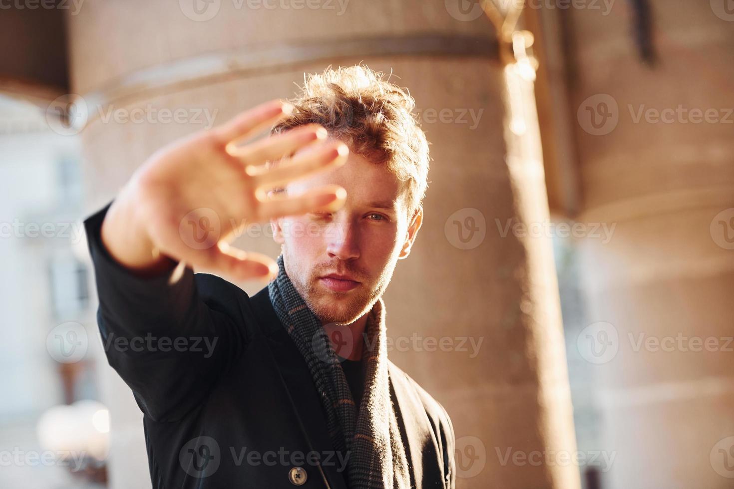 Shows stop gesture by the hand. Elegant young man in formal classy clothes outdoors in the city photo