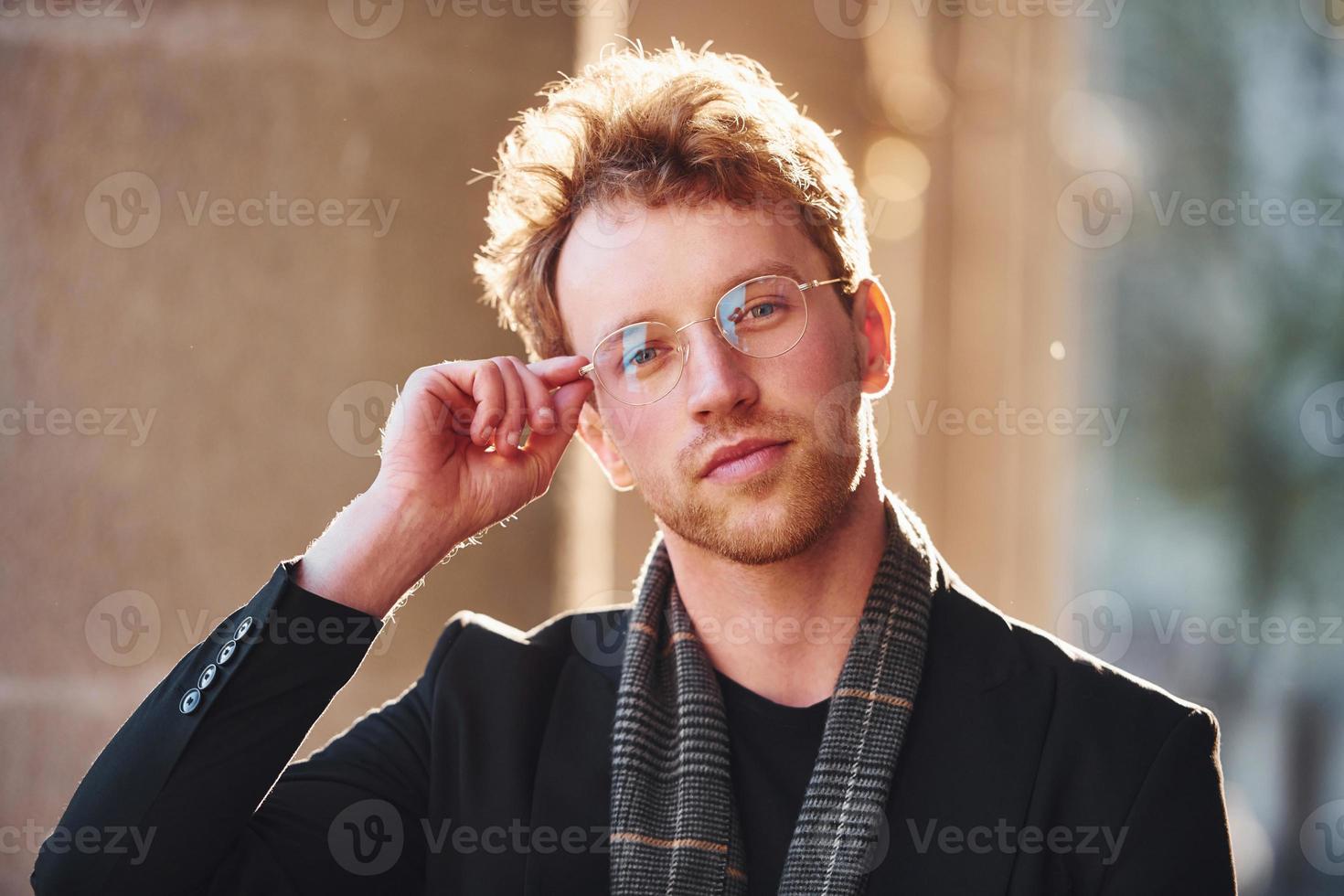 Portrait of elegant young man in glasses and formal classy clothes outdoors in the city photo