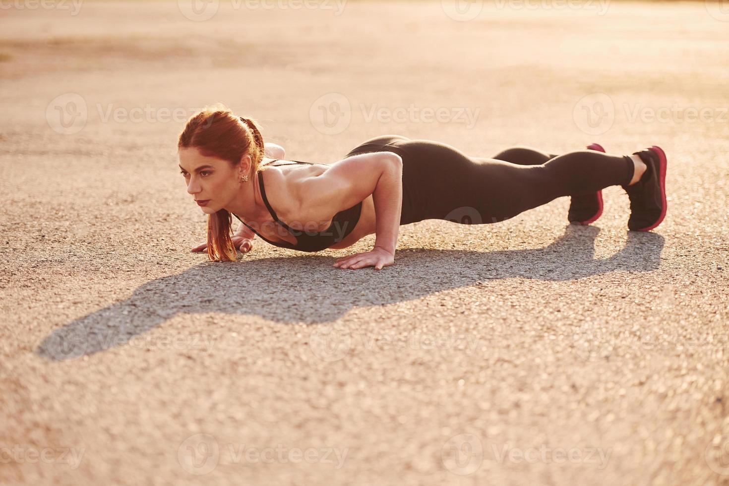 Woman in sportswear doing push-ups on the road at evening time photo