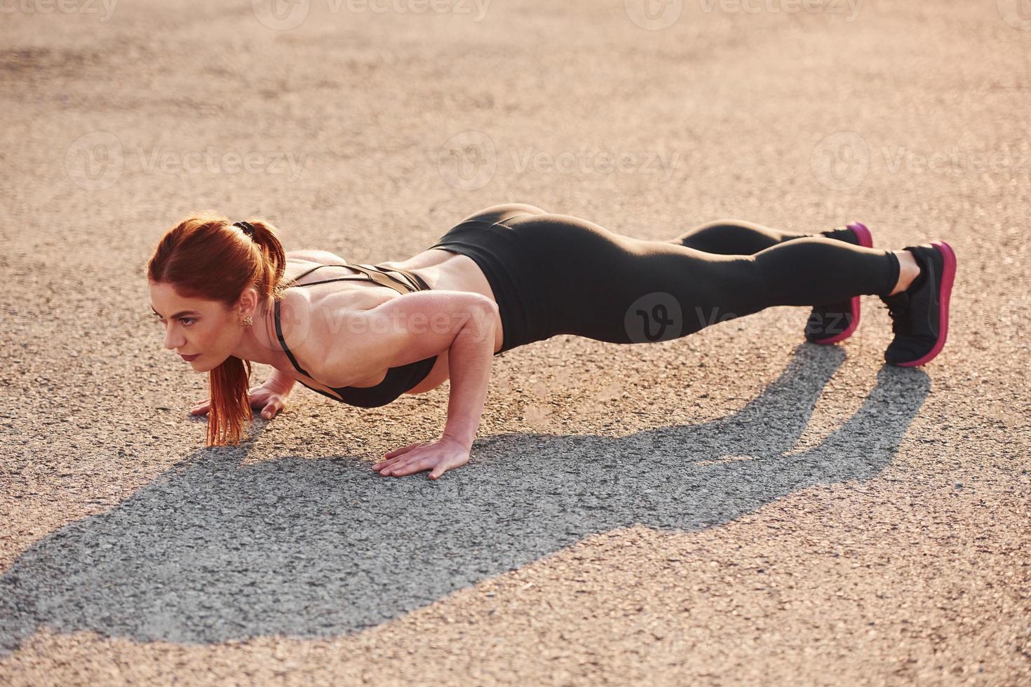 mujer en ropa deportiva haciendo flexiones en la carretera al atardecer foto