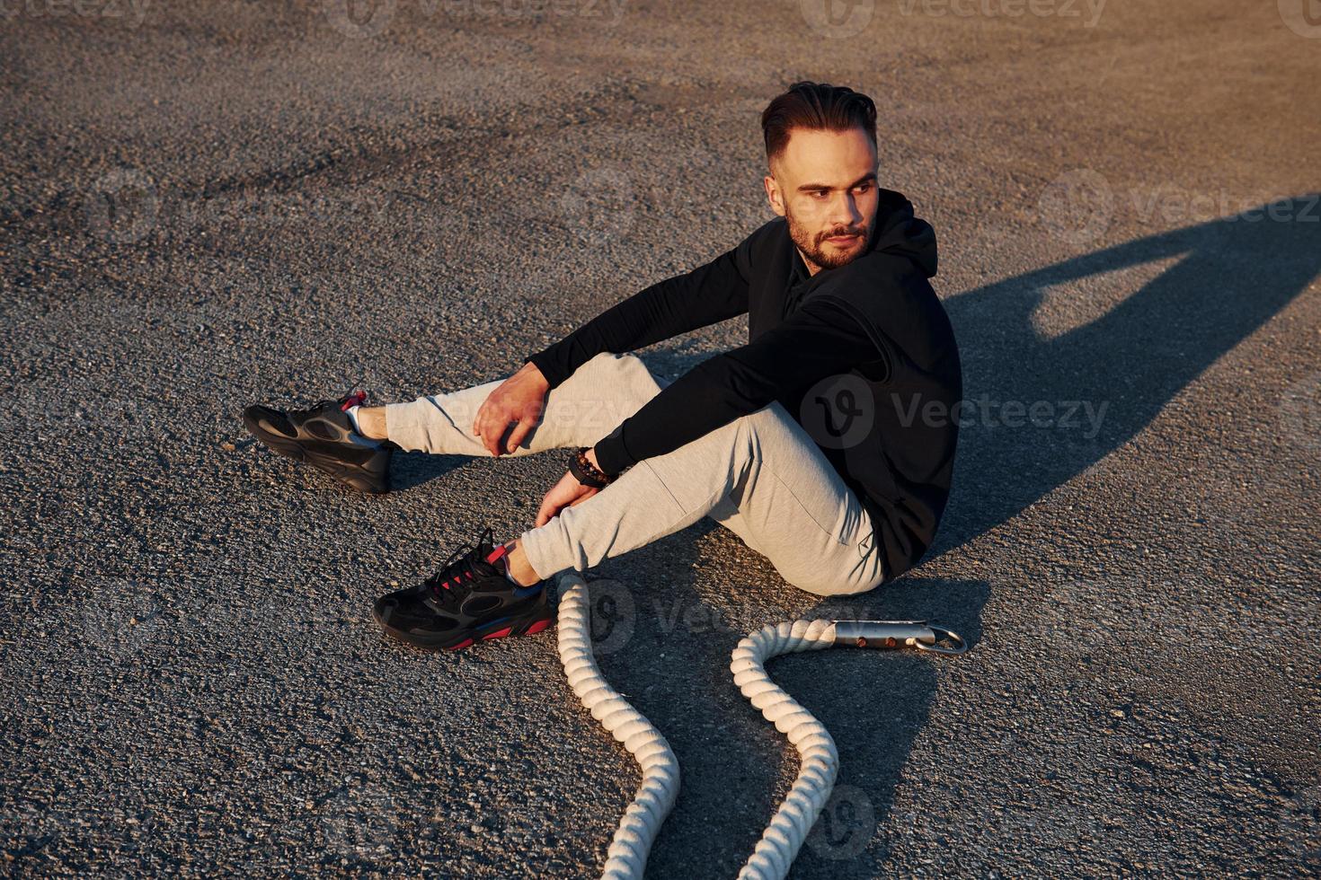 Man in sportswear sitting on the road at evening time with ropes and resting photo