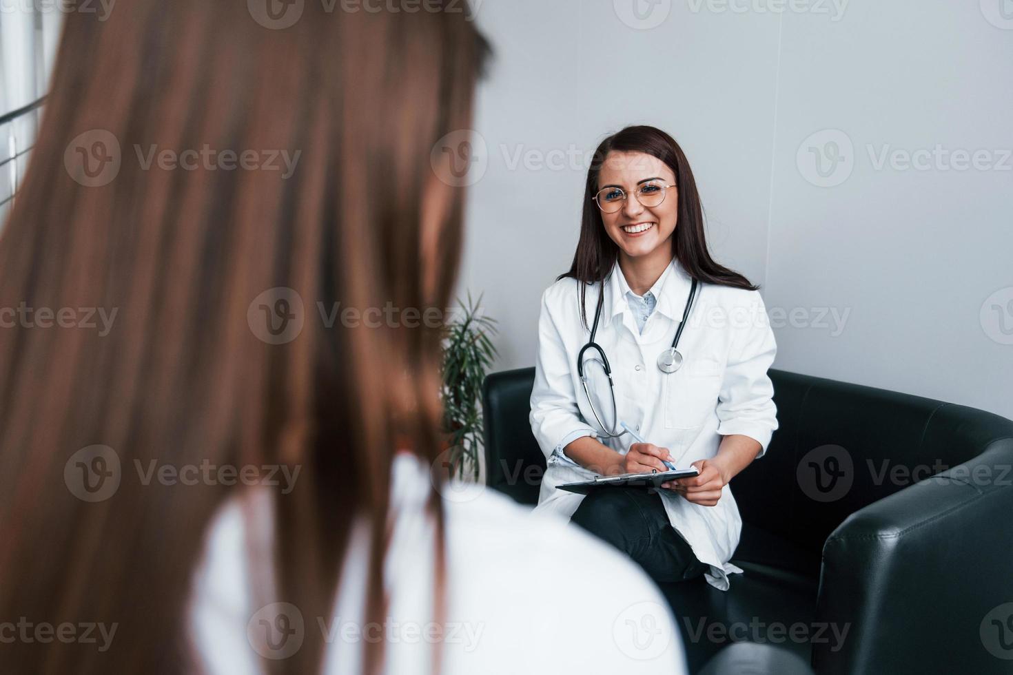 Sitting and talking. Young woman have a visit with female doctor in modern clinic photo