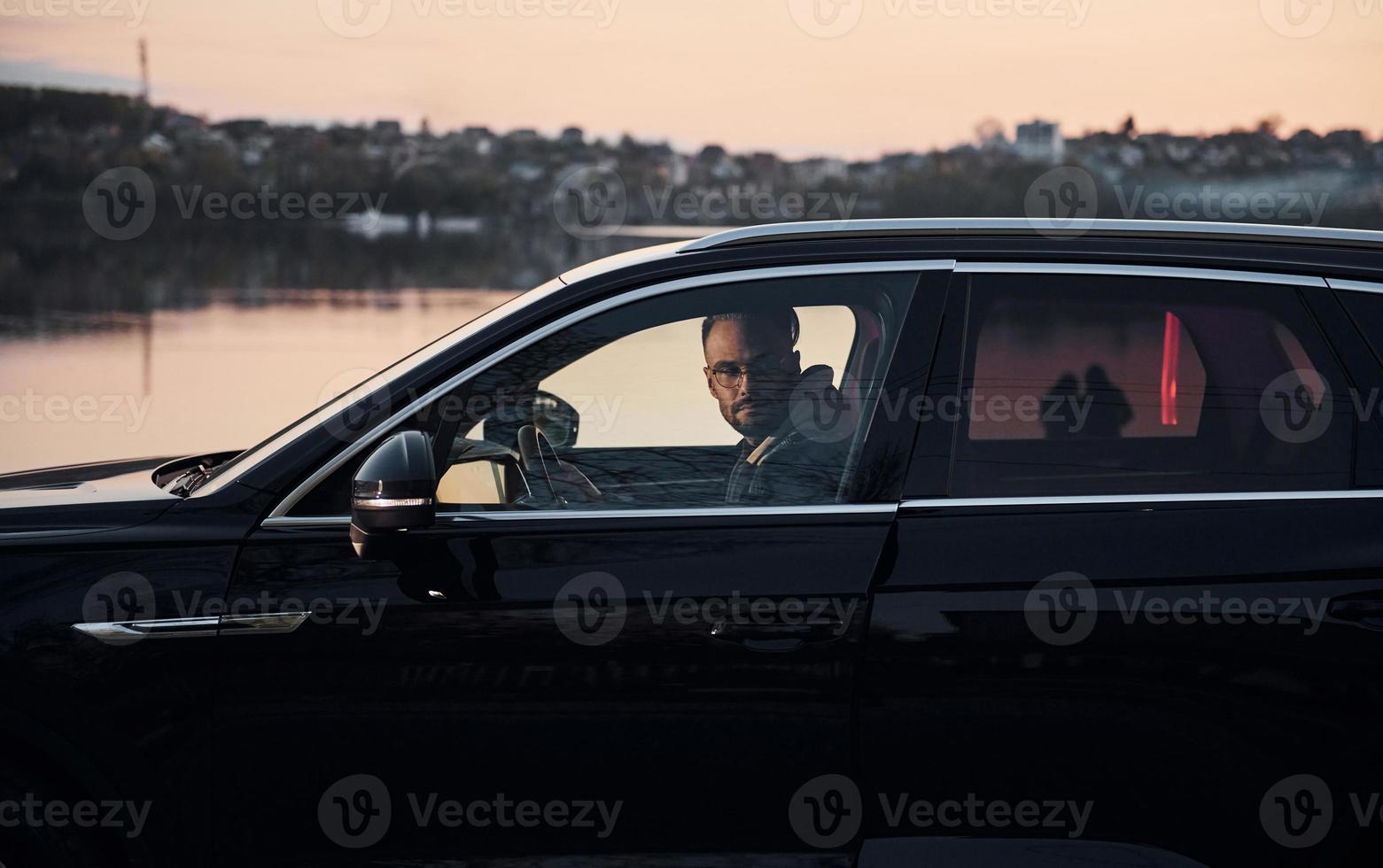 vista lateral de un apuesto hombre sin afeitar con ropa de moda que monta su automóvil foto