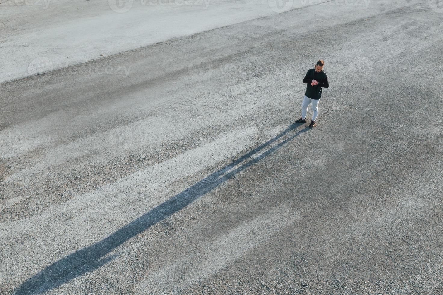 Top view of man that standing on the road at evening alone and looking at watch photo