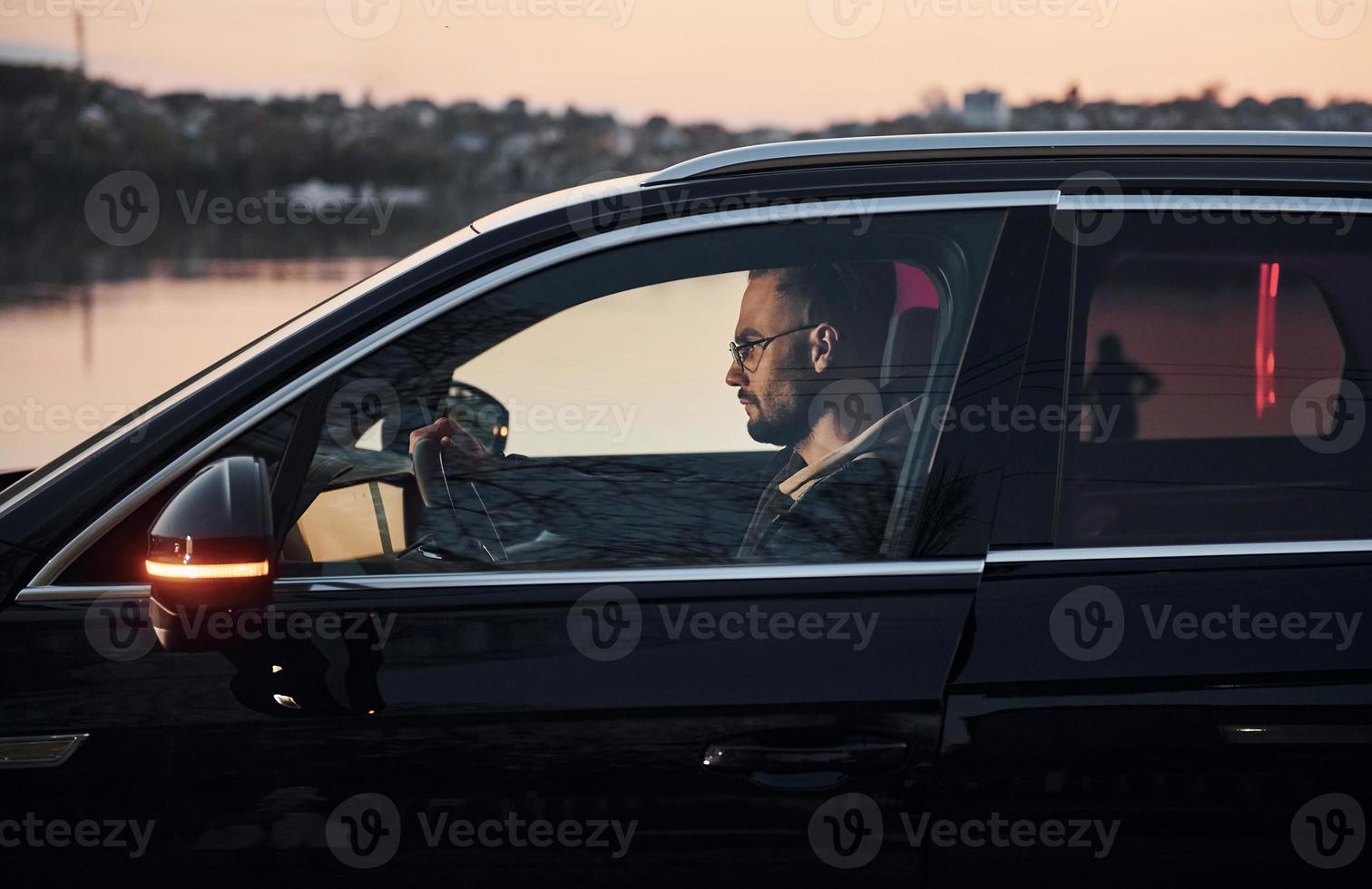 Side view of handsome unshaved man in fashionable clothes that riding his automobile photo