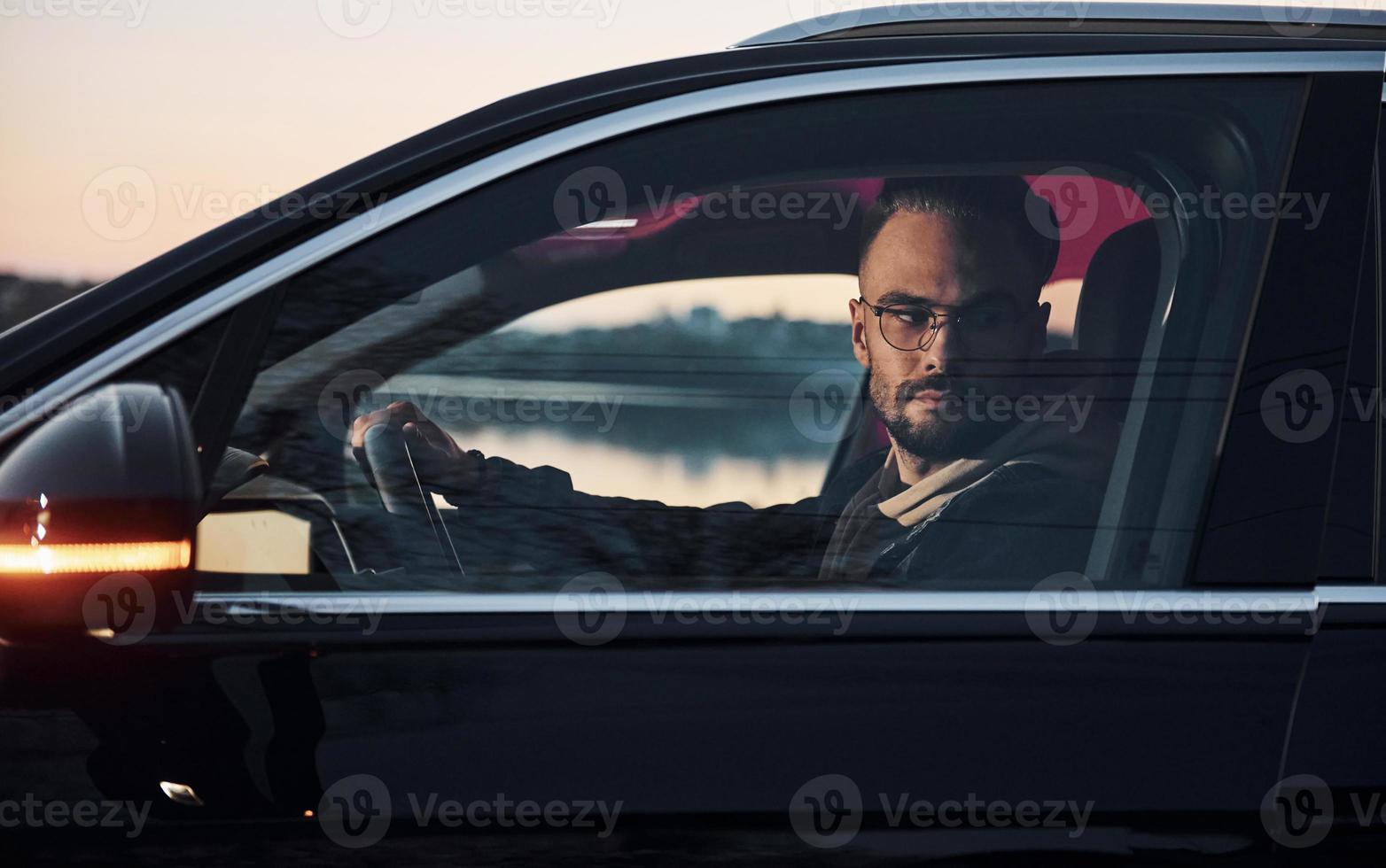 Side view of handsome unshaved man in fashionable clothes that riding his automobile photo