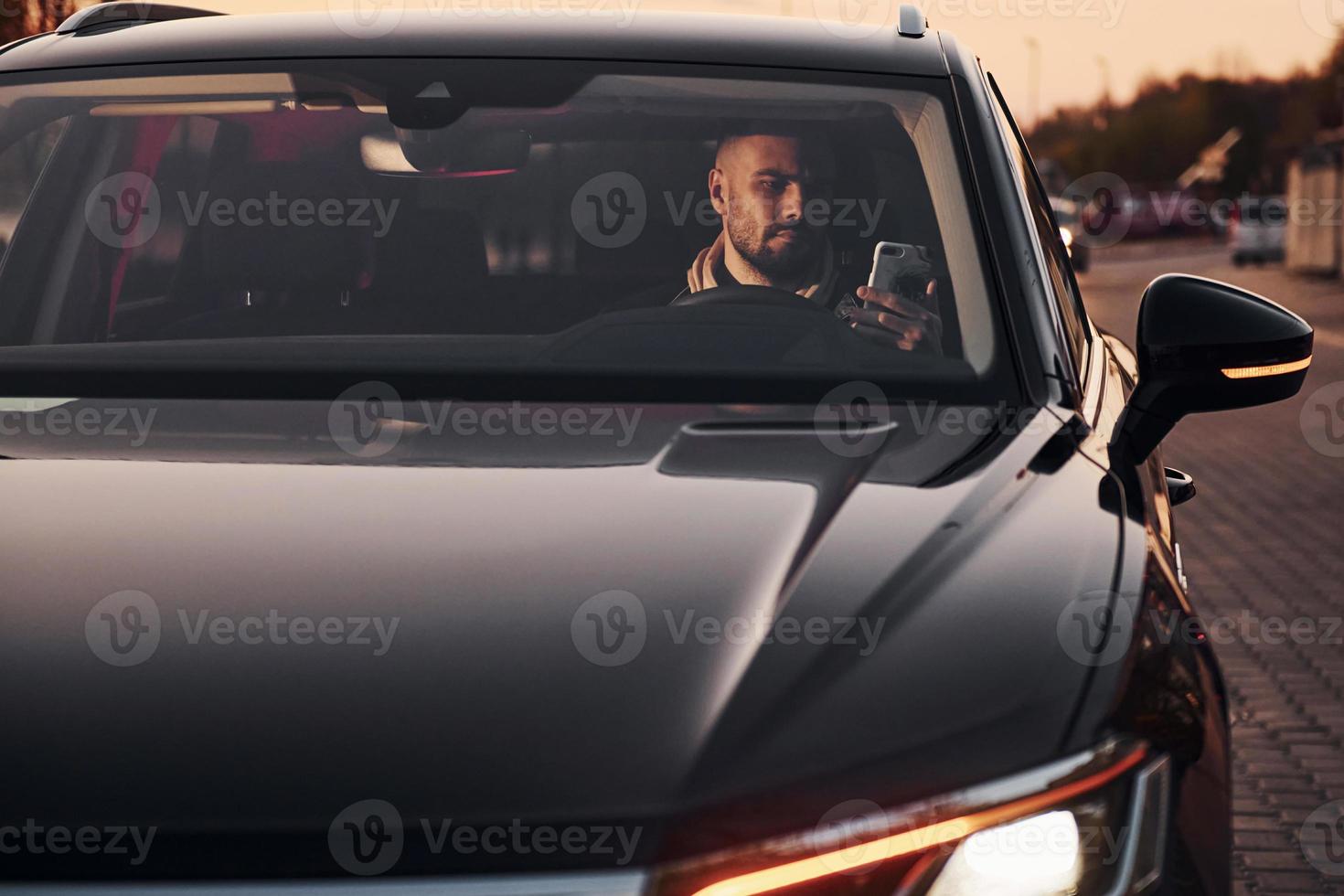 Front view of handsome unshaved man in fashionable clothes that riding his automobile photo