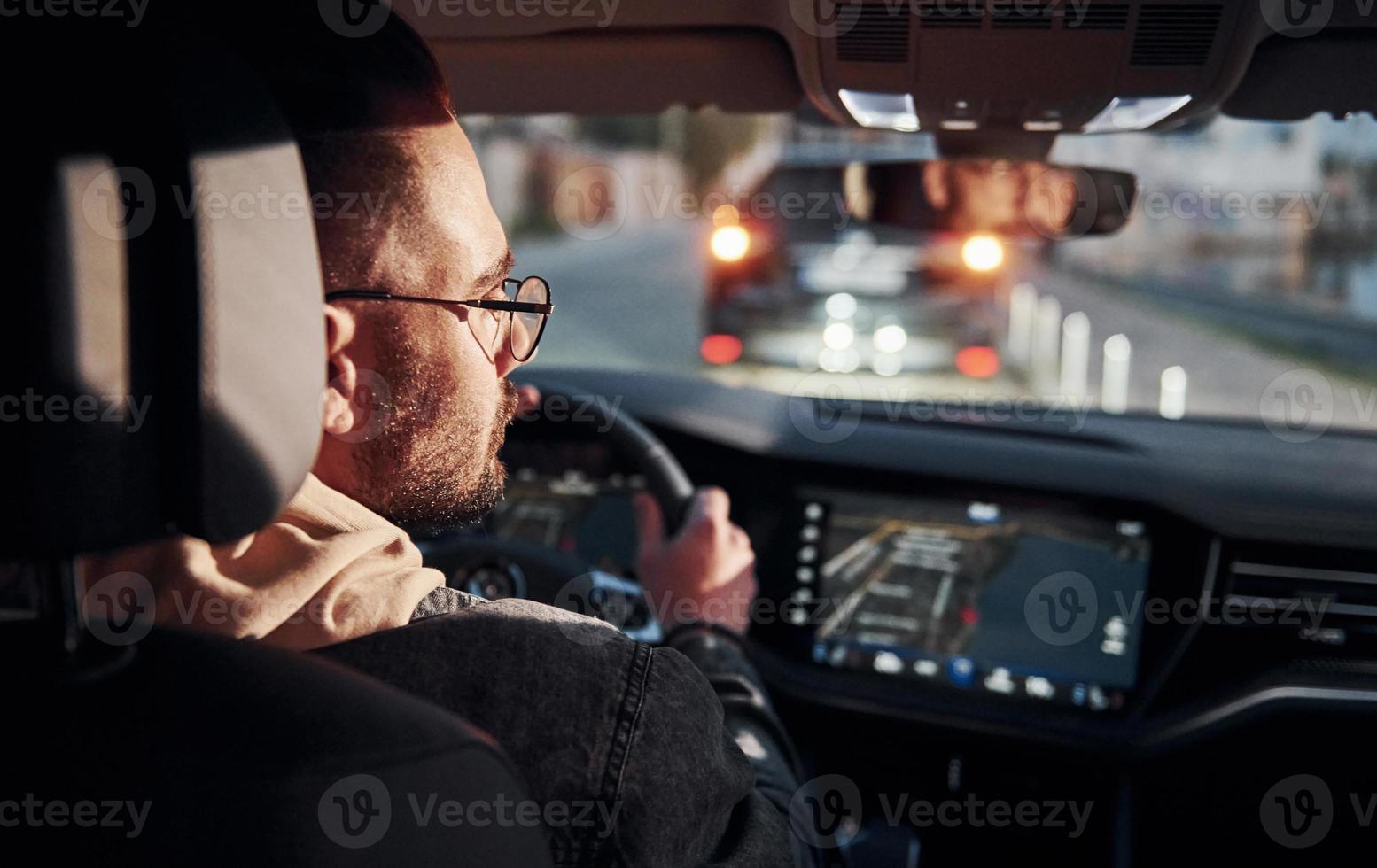 Rear view of handsome unshaved man in fashionable clothes that riding his automobile photo