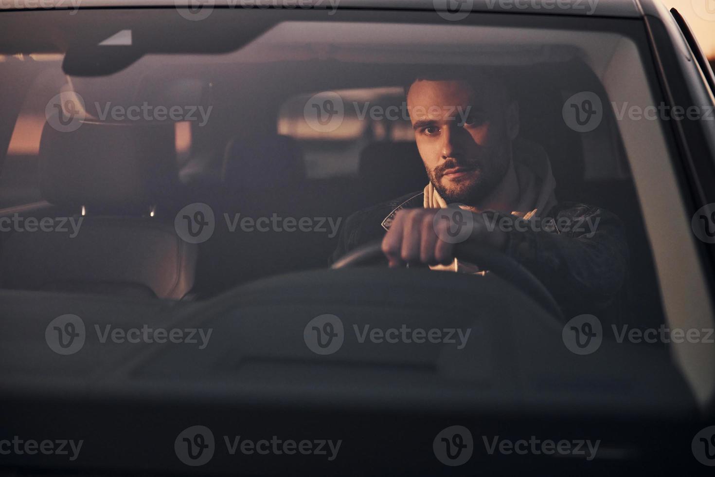 Front view of handsome unshaved man in fashionable clothes that riding his automobile photo