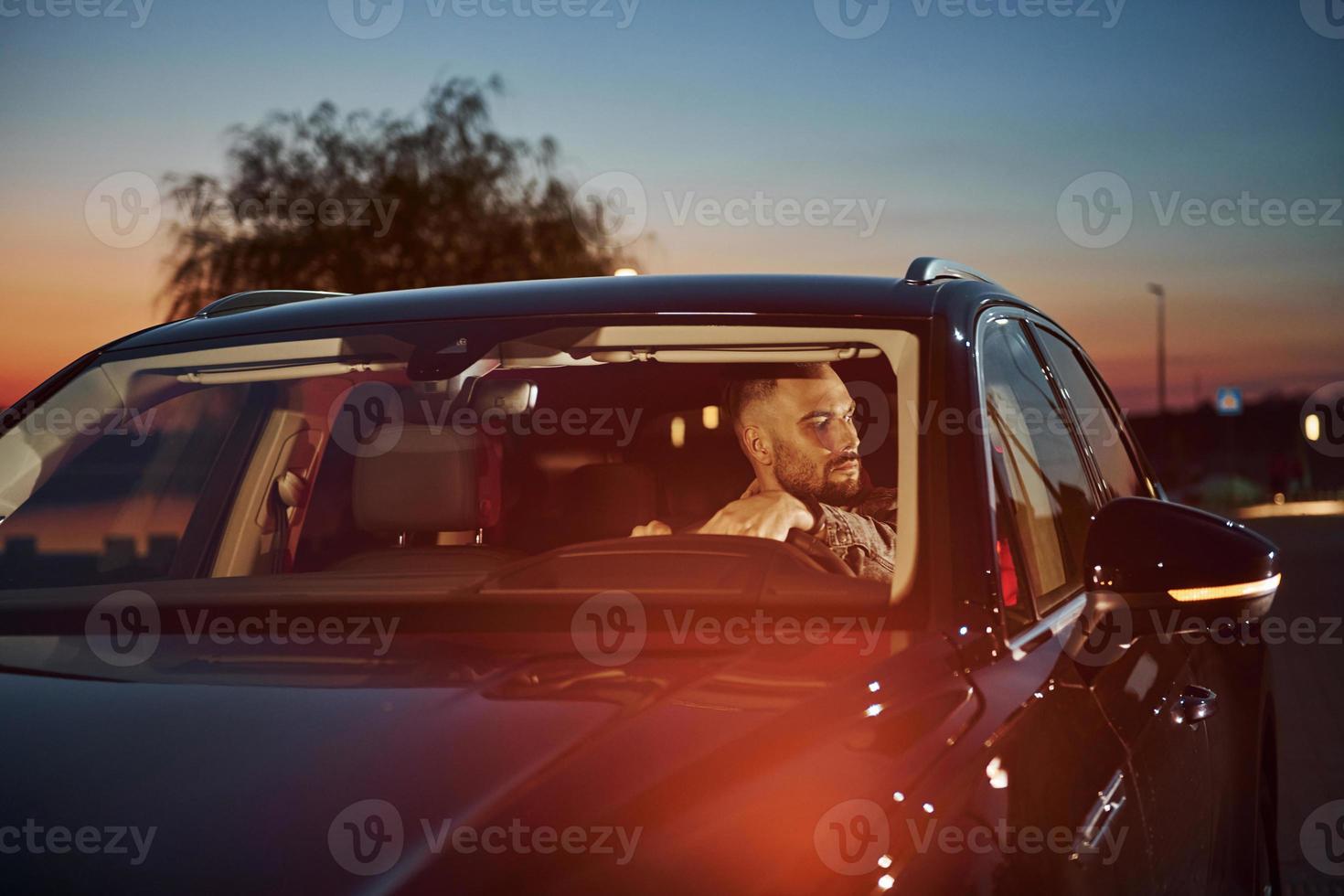 Handsome unshaved man in fashionable clothes riding his automobile photo