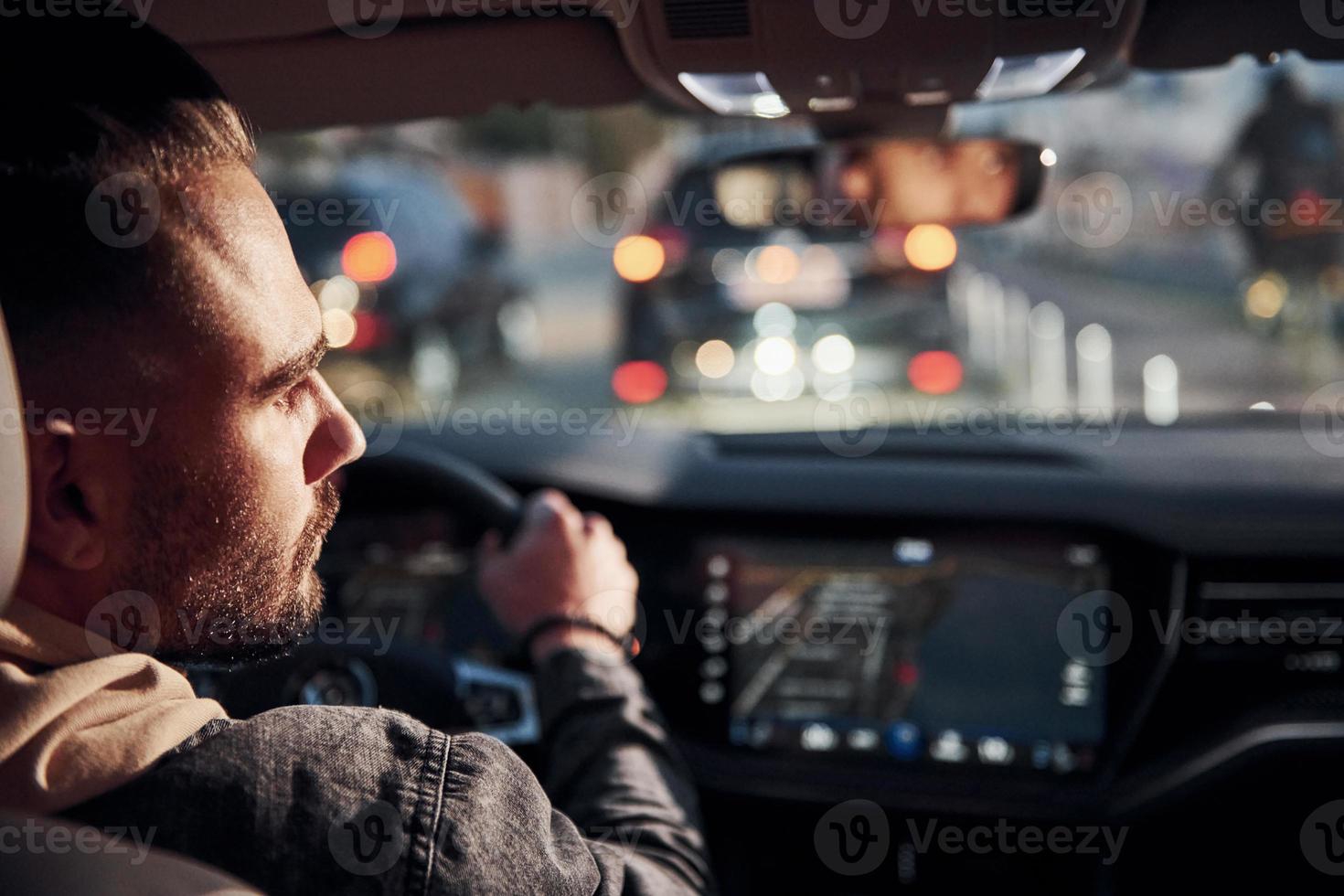 Rear view of handsome unshaved man in fashionable clothes that riding his automobile photo