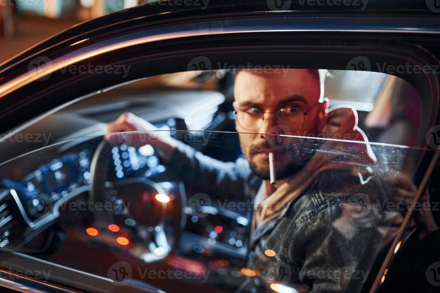 Smoking cigarette. Handsome unshaved man in fashionable clothes riding his automobile photo