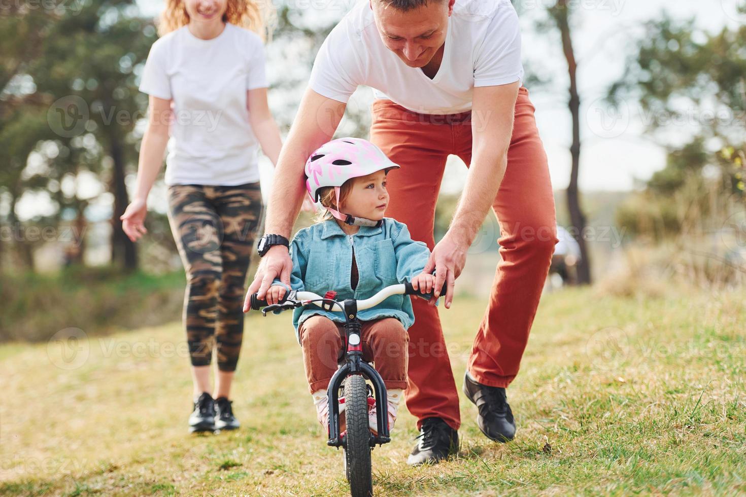 Mother and father teaching daughter how to ride bicycle outdoors photo