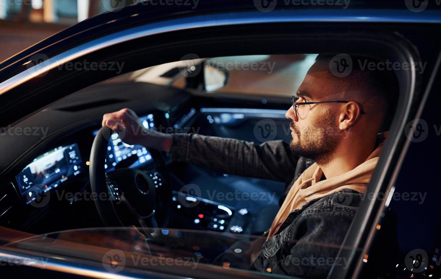 Side view of handsome unshaved man in fashionable clothes that riding his automobile photo