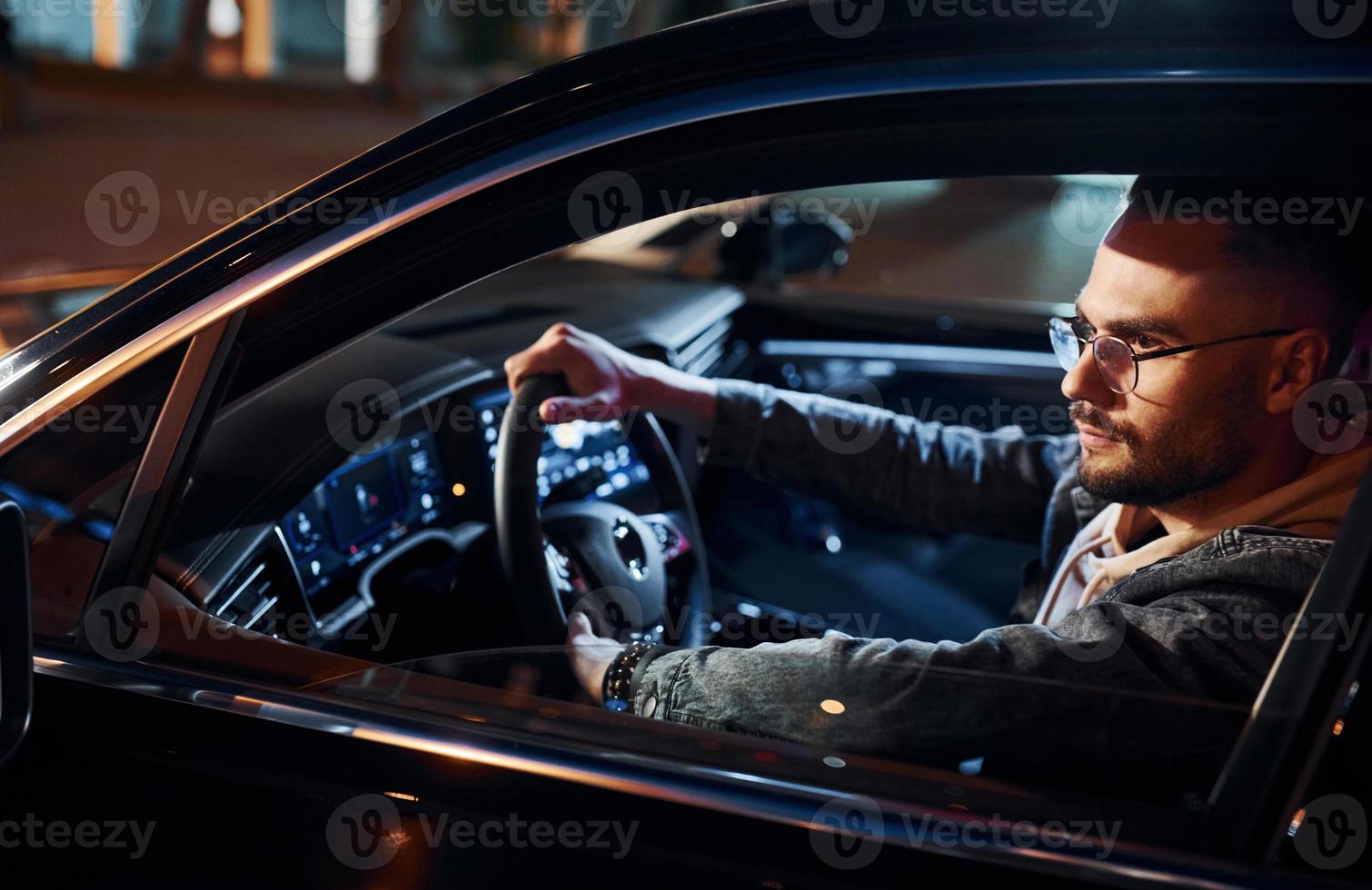 Side view of handsome unshaved man in fashionable clothes that riding his automobile photo