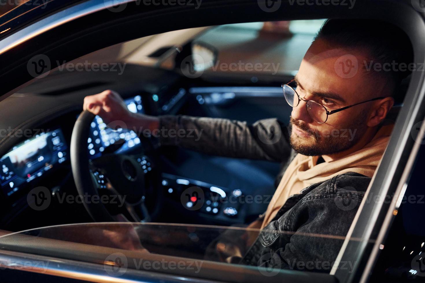 Side view of handsome unshaved man in fashionable clothes that riding his automobile photo