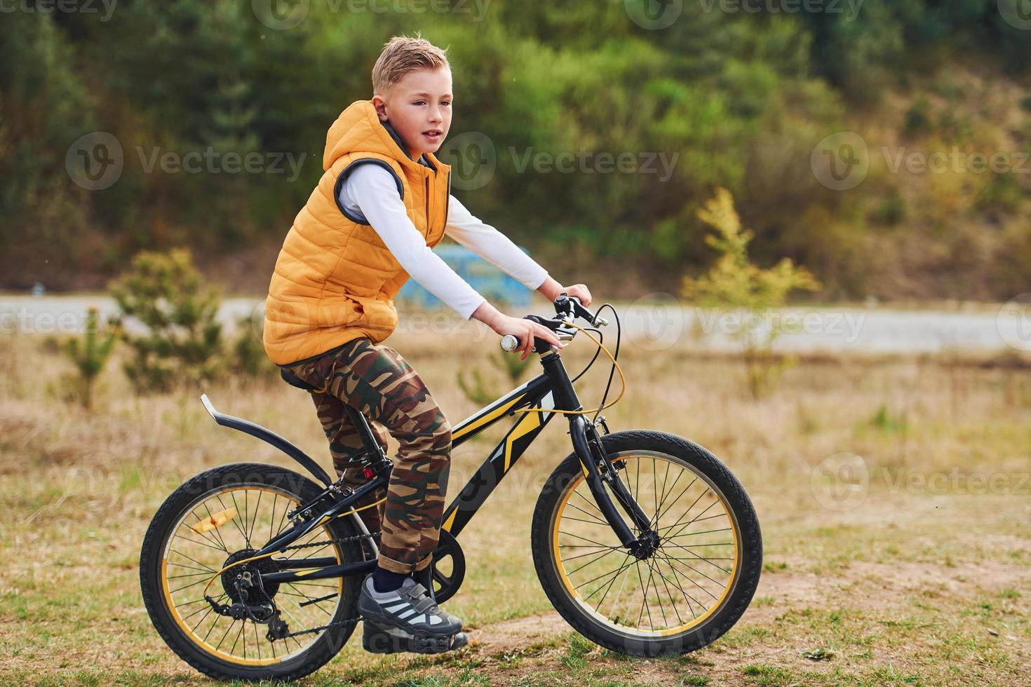 Young boy in orange colored jacket sitting on his bike outdoors at daytime photo