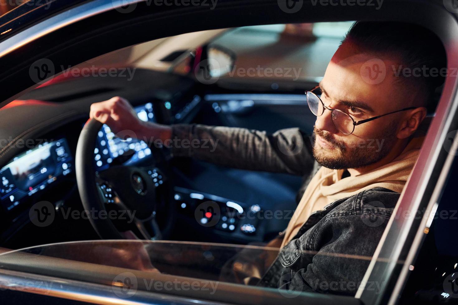 Side view of handsome unshaved man in fashionable clothes that riding his automobile photo