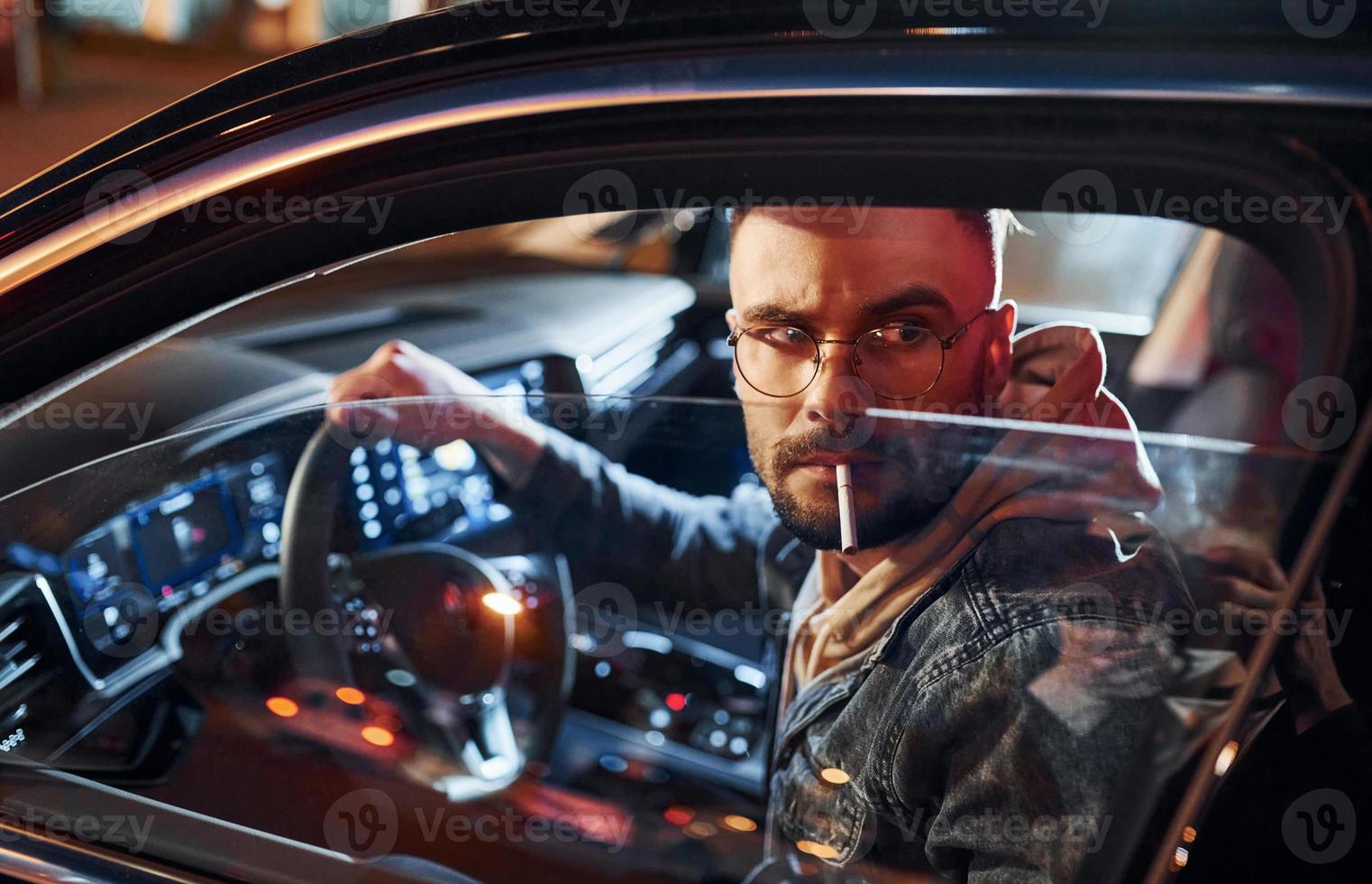 Smoking cigarette. Handsome unshaved man in fashionable clothes riding his automobile photo