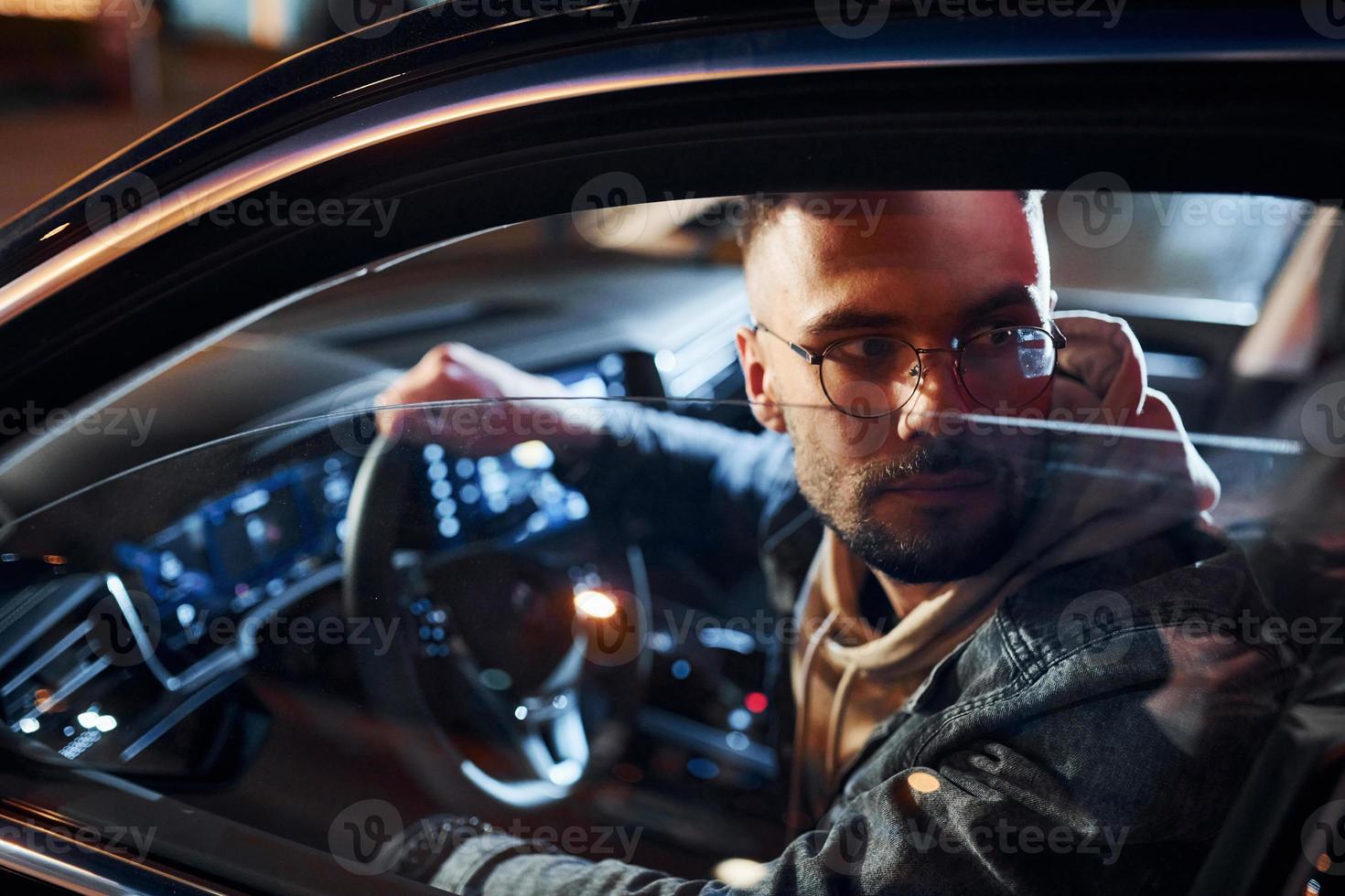 Side view of handsome unshaved man in fashionable clothes that riding his automobile photo