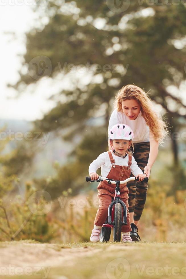 Mother in white shirt teaching daughter how to ride bicycle outdoors photo