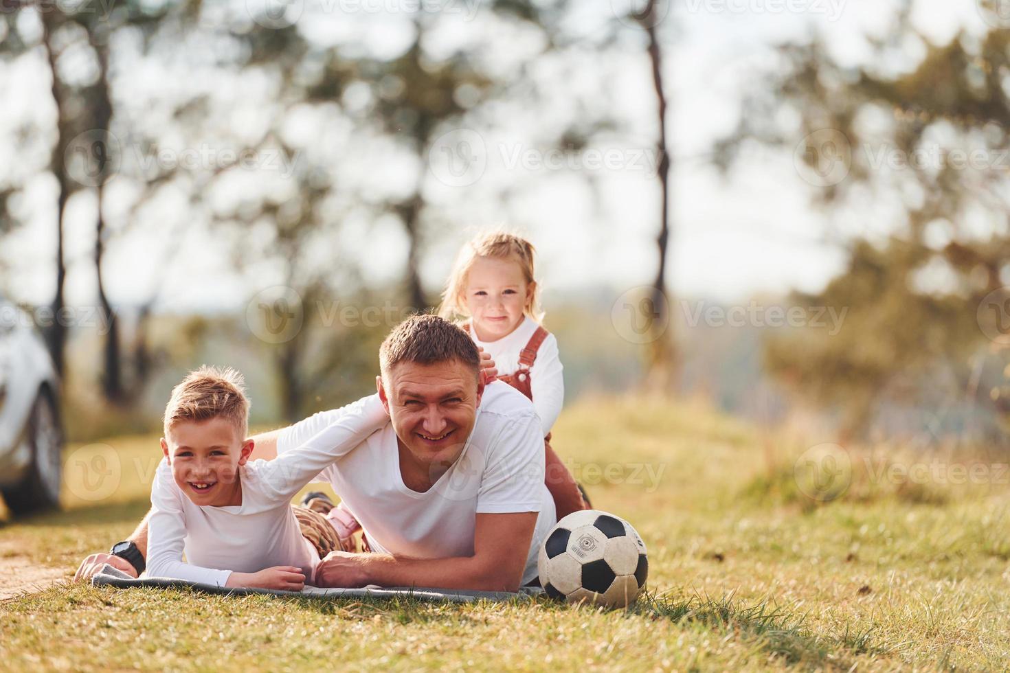 Father with his little daughter and son lying down on the ground outdoors near the forest photo