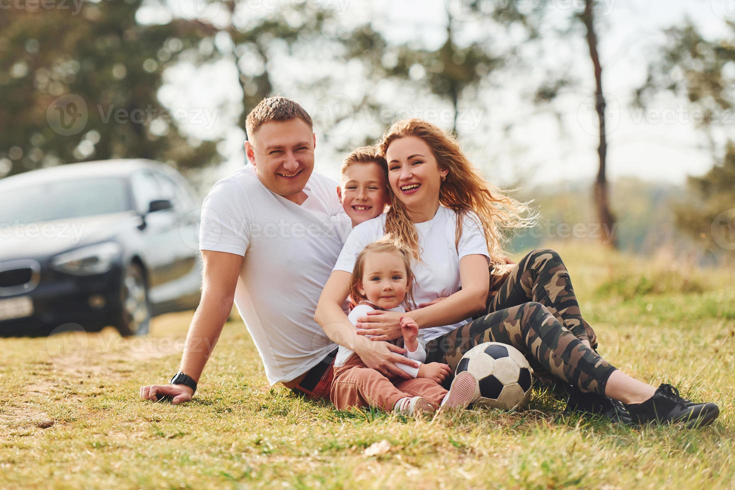 Sitting and lying on the ground. Happy family spending weekend together outdoors near the forest. With daughter and son photo