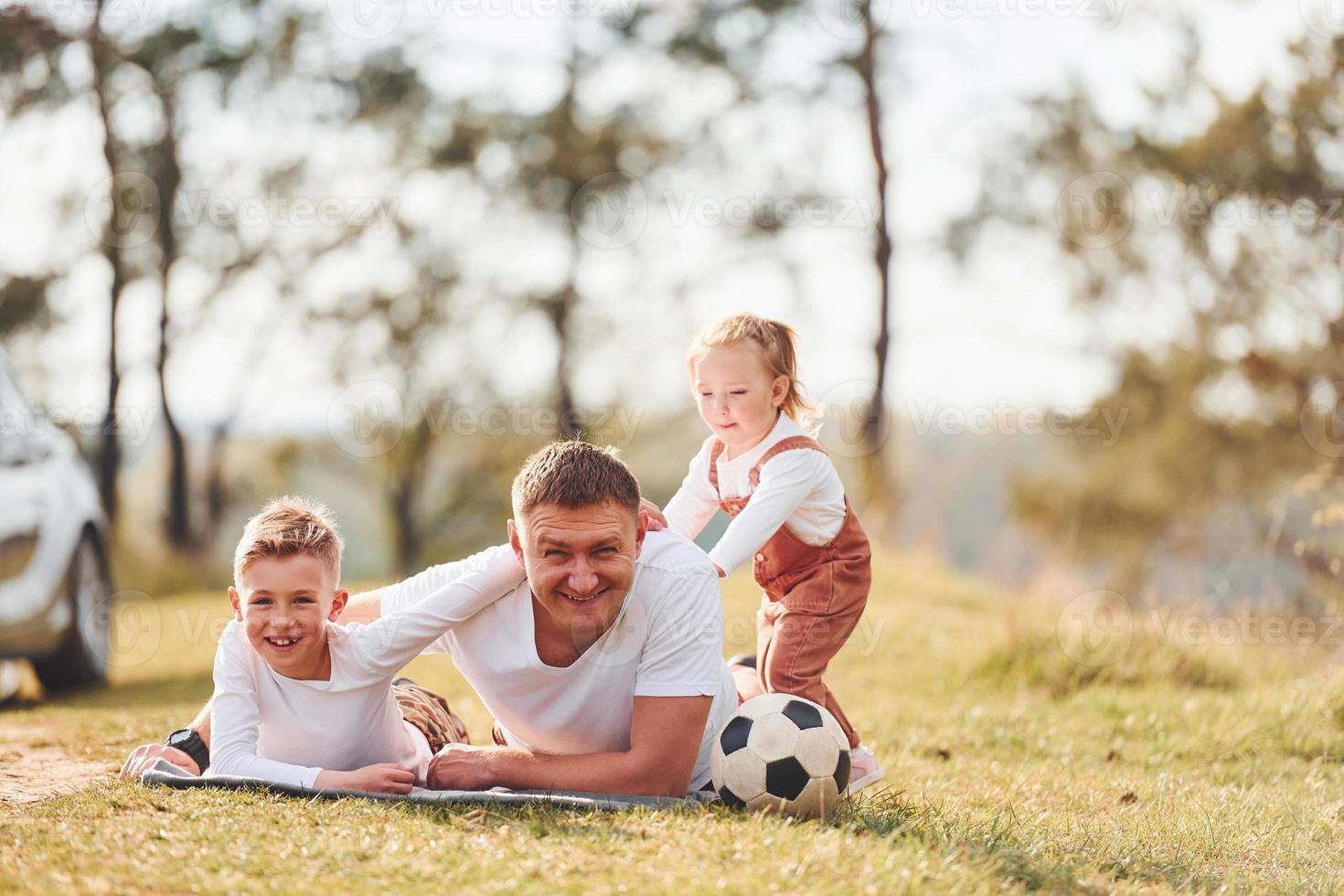 Father with his little daughter and son lying down on the ground outdoors near the forest photo