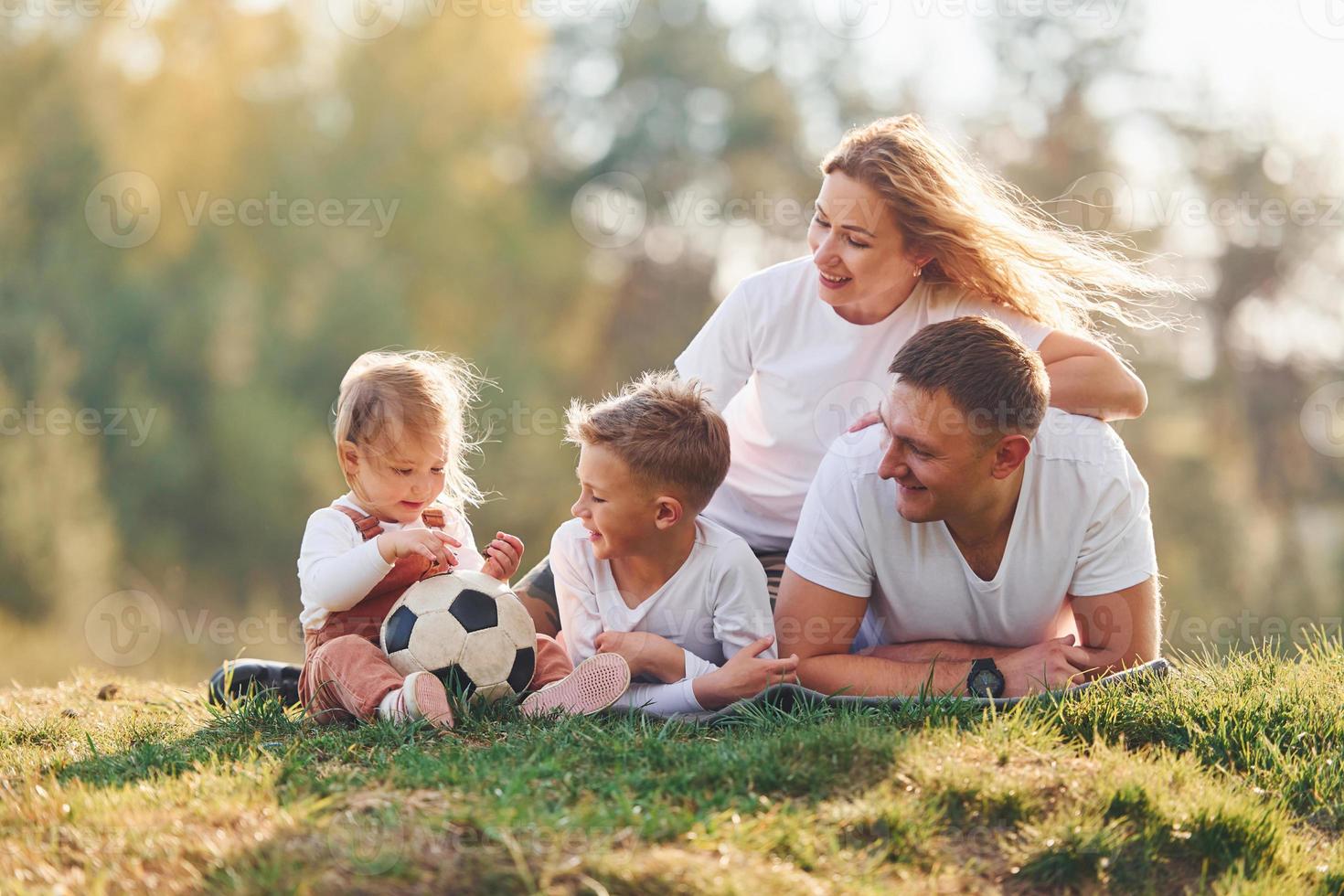 With soccer ball. Happy family lying down outdoors near the forest. With daughter and son photo