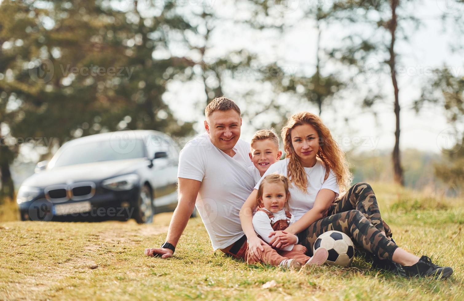 Sitting and lying on the ground. Happy family spending weekend together outdoors near the forest. With daughter and son photo