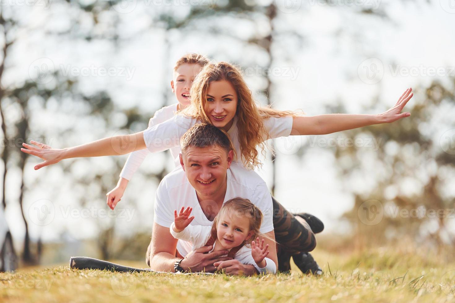 Sitting and lying on the ground. Happy family spending weekend together outdoors near the forest. With daughter and son photo