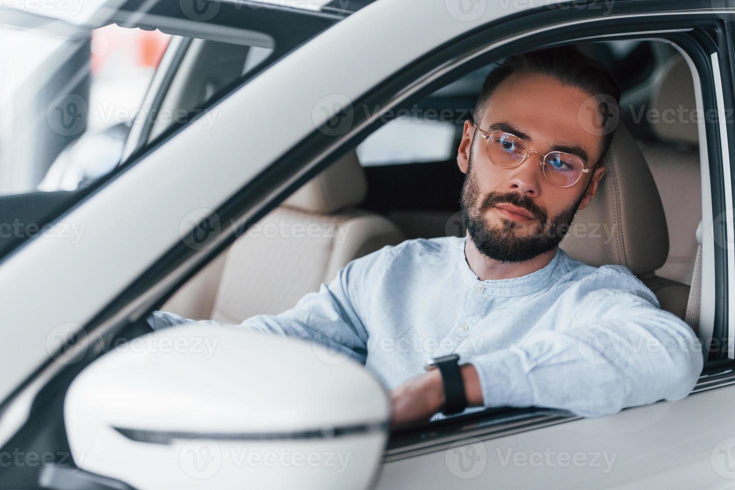 Side view of young handsome man in formal clothes that sitting in brand new automobile photo