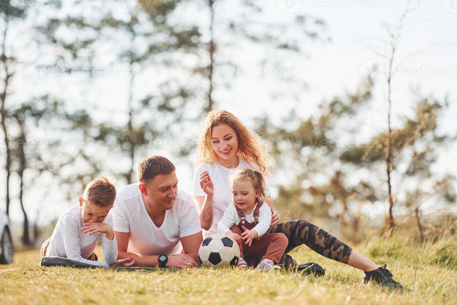 Sitting and lying on the ground. Happy family spending weekend together outdoors near the forest. With daughter and son photo