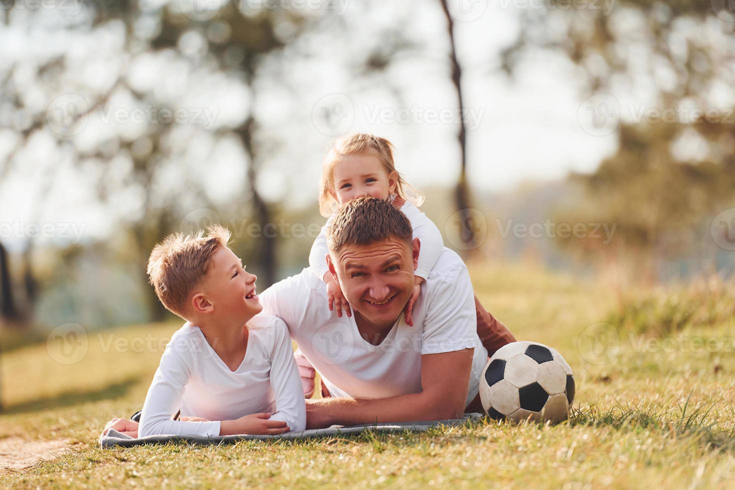 Father with his little daughter and son lying down on the ground outdoors near the forest photo