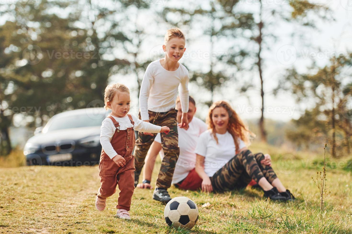 Happy family playing with soccer ball outdoors near the forest. With daughter and son photo