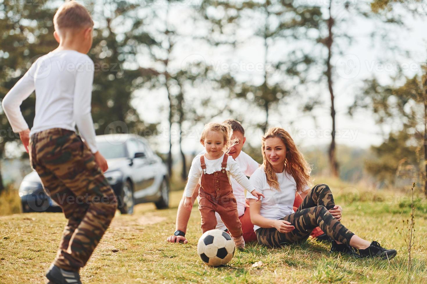 Happy family playing with soccer ball outdoors near the forest. With daughter and son photo