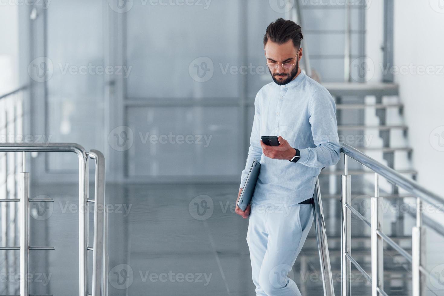 Using phone. Young handsome man in formal clothes indoors in the office at daytime photo